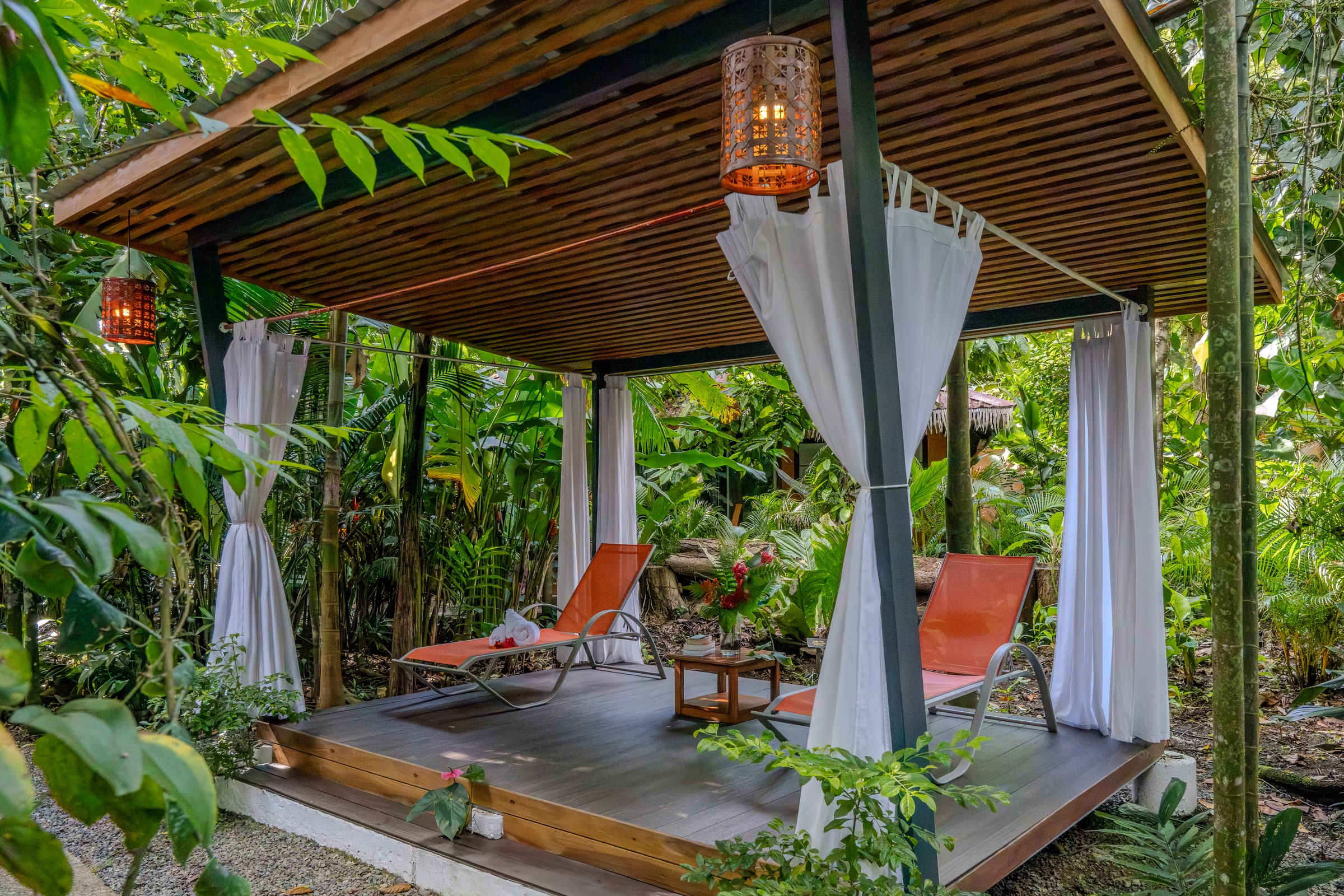 Shaded wooden deck with a lounger and linen curtains among the plants