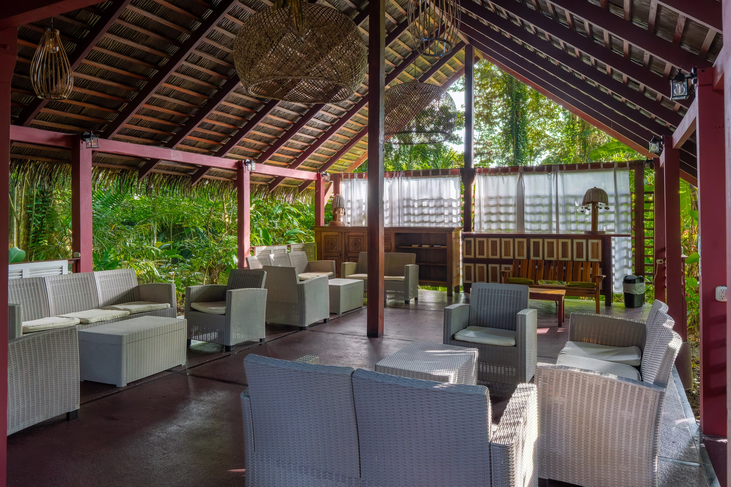 Covered lounge with white wicker sofas under a thatched roof at Namuwoki Lodge